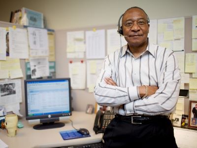 man with headset at desk smiling a camera